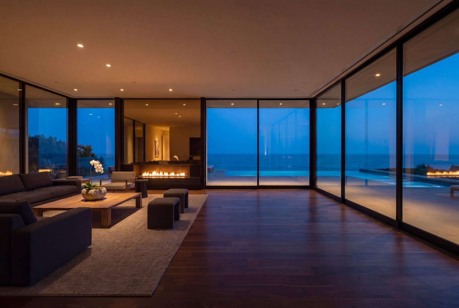 Twilight interior of a luxury coastal California estate with floor-to-ceiling glass walls and Pacific Ocean view